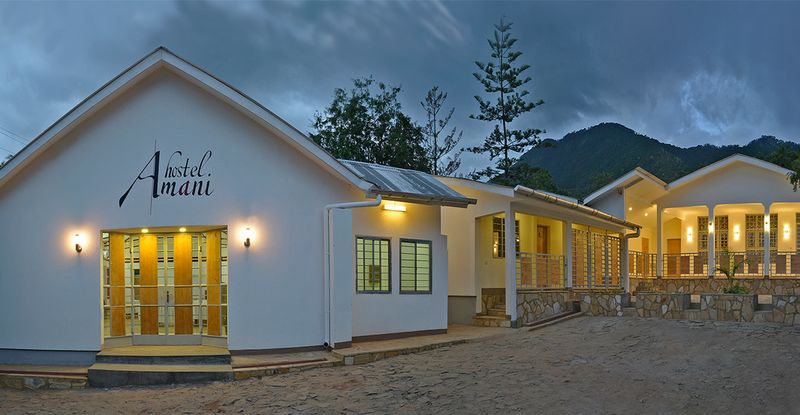 White building with lit entrance at dusk, mountains behind